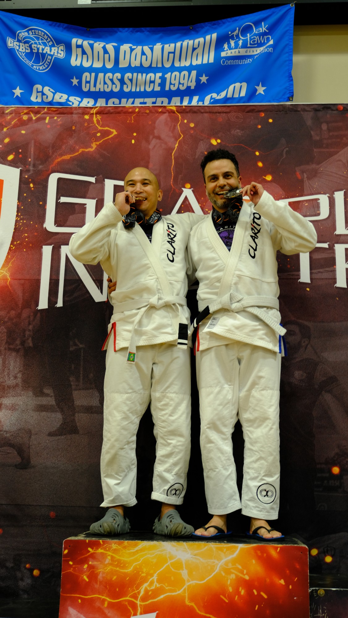 Two Project Clarito students on the podium after a BJJ competition, medals in hand.